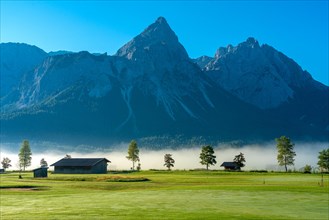 Lawn and meadow in morning fog in the valley of the Wetterstein range with the peak of the Sonnenspitze
