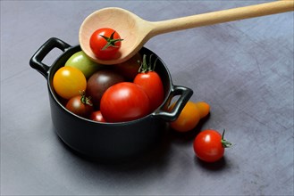 Different cherry tomatoes in pot with cooking spoon