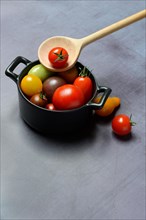 Different cherry tomatoes in pot with cooking spoon