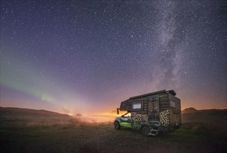 Night shot of a painted camper van under the Milky Way with northern lights