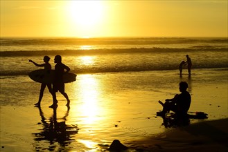 People on the beach with surfboard at sunset