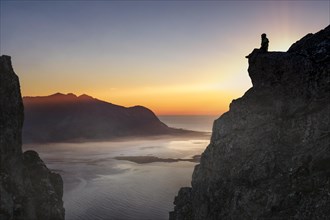 Silhouette of a woman sitting on a rocky outcrop at sunset