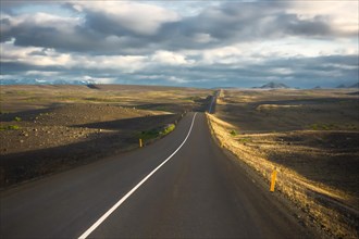 Road in the evening light runs through vuclan plateau with lava rock in the Krafla