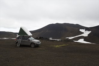 Off-road vehicle with roof tent and ladder on barren plateau
