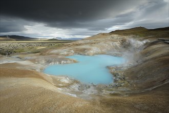 Turquoise lake with dramatic clouds in the lava river Leihrnjukur in the Krafla