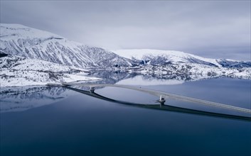 Long car bridge over a mirror-smooth blue fjord in a winter landscape