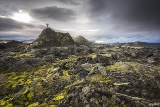 Man on a hill in a black lava field with green moss stretching hands into the dramatic sky