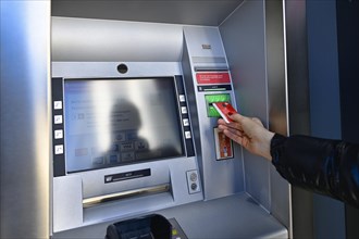Woman introduces ec-card at the cash dispenser of a savings bank