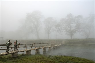 Two men walk in the morning fog over a bridge over the Rapti River