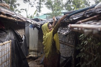 Rohingya woman covers the roof of her hut with a carpet to keep the interior dry during the heavy monsoon rains