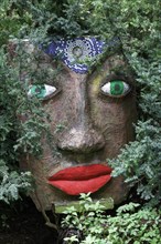 Magical woman face with red lips and green eyes looks through branches