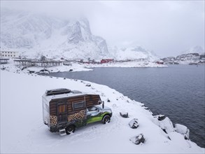 Motorhome painted as an alpine hut in snowfall at the parking lot in front of Reinefjord