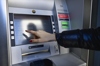 Woman typing on the touch screen of an ATM of a savings bank