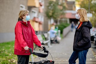 Senior citizen with walker and granddaughter in front of a retirement home wearing mouth protection against corona viruses