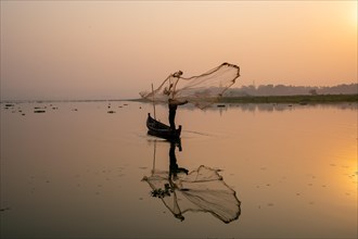 Fisherman with boat on Taung Tha Man Lake casts a fishing net for sunrise