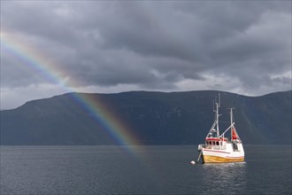 Fishing boat in fjord with rainbow