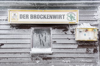 Shield The Brockenwirt on snow-covered wooden facade with window