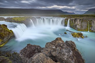 Long time exposure of a turquoise waterfall in volcanic landscape with dramatic clouds
