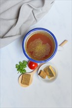 Cup with bouillon broth and bouillon cubes on a wooden spoon