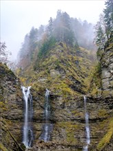 Waterfalls tumble over a rock face in the autumnal mountain forest near Hochnebel