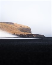 Yellow grassy mountain with black sand and waves in the foreground