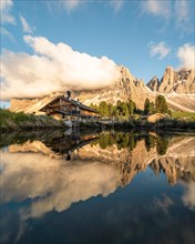 Reflection from the Furchetta mountain and the Geisler Alm hut in a pond near the Geisler Alm at sunset