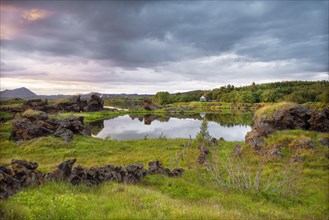 Lava formations of volcanic rock rise from green meadows with dramatic skies at Kalfastroend