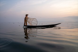 Traditional fisherman posing standing on his small boat in front of sunrise