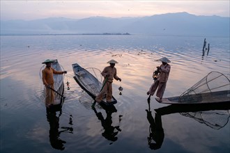 Three traditional fishermen stand with lamps on their small boats