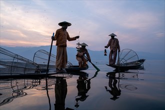 Three traditional fishermen sit and stand with lamps on their small boats