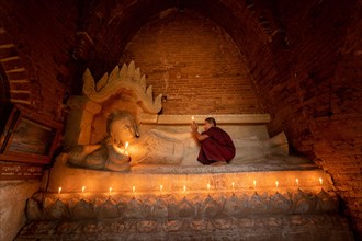 Buddhist young monk in red robe with red umbrella praying with candle in hand in a temple