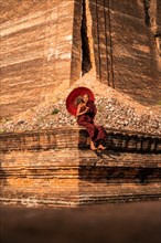 Buddhist monk sitting with red umbrella in front of Mingun Pagoda