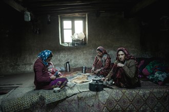 A woman with an infant and two other woman sitting on carpets in the living room of a traditional mud house