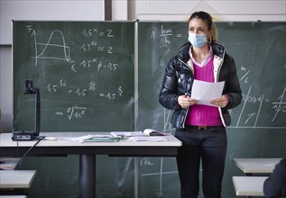 Teacher with winter jacket and face mask in classroom teaching