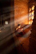 Buddhist young monk in red robe sits and reads rays of light in a temple