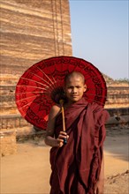 Buddhist monk stands with red umbrella in front of Mingun Pagoda
