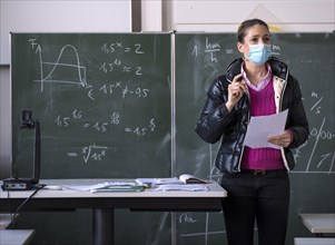 Teacher with winter jacket and face mask in classroom teaching