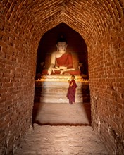 Buddhist young monk in red robe praying standing in a temple