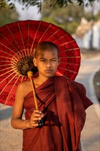 Buddhist monk stands with red umbrella on a path