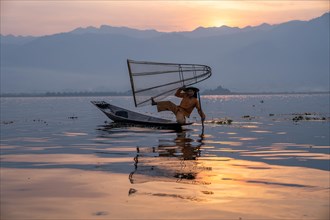 Traditional fisherman poses sitting on his small boat in front of sunrise