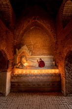 Buddhist young monk in red robe with red umbrella praying with candle in hand in a temple