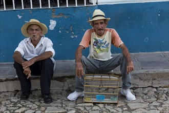 Two older Cubans with cigars and songbird in a cage