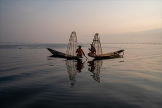 Two traditional fishermen pose sitting on their small boats