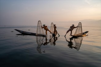 Three traditional fishermen pose standing on their small boats