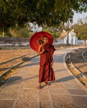 Buddhist monk stands with red umbrella in front of the path of the Hsinbyume pagoda with frame