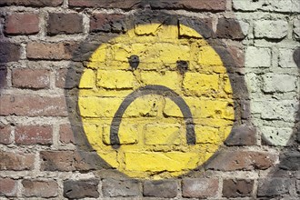 Yellow sad smiley painted on a brick wall