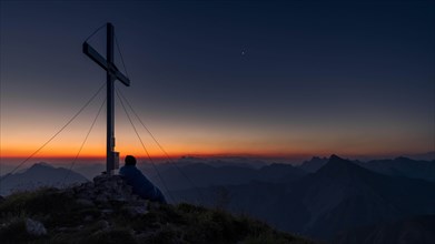 Cross of the Kreuzspitze at sunrise with mountaineer at the summit