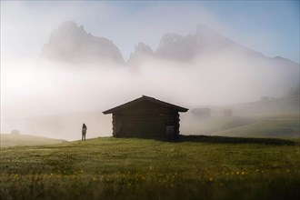 Woman looking on foggy meadow next to hut
