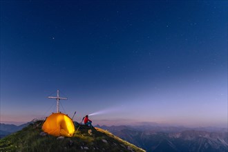 Cross of the Kreuzspitze by a starry sky with tent and mountaineer at the summit