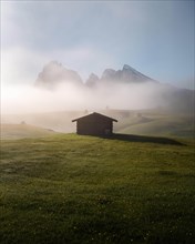 Hay barn and huts on foggy meadows in front of Sassolungo and Plattkofel